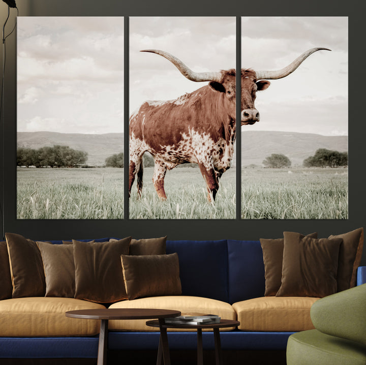 Canvas of a Texas longhorn standing in a grassy field with mountains in the background, ideal for rustic or country-style western wall decor.