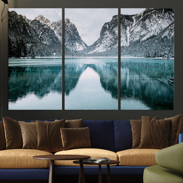 Crystal-clear alpine lake reflecting snow-covered mountains, surrounded by evergreen trees, creating a serene and tranquil winter landscape.