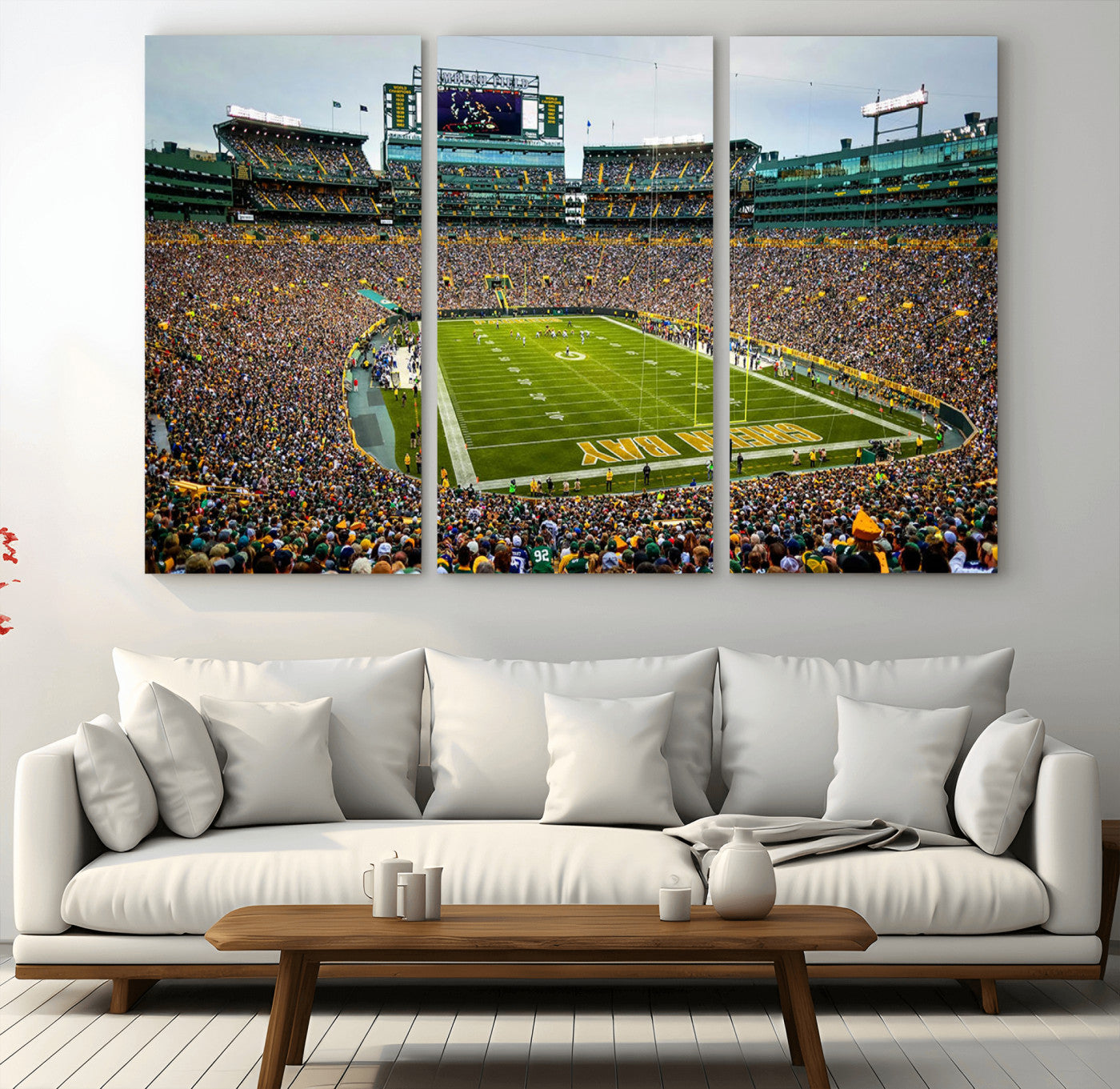 Packed football stadium with thousands of fans watching an American football game on a well-maintained field. The scoreboard displays "Lambeau Field," and players are lined up on the field. The stadium is surrounded by multiple tiers of seating filled wit