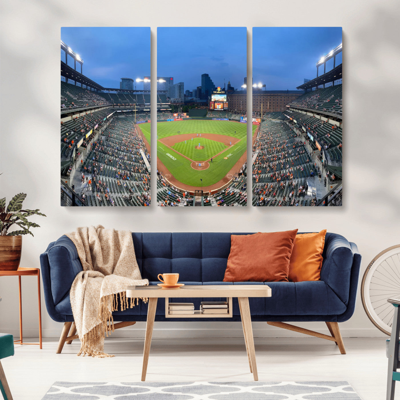 Wide panoramic view of a baseball stadium at dusk with players on the field, stadium lights illuminating the scene, and a sparse crowd of spectators in the stands.