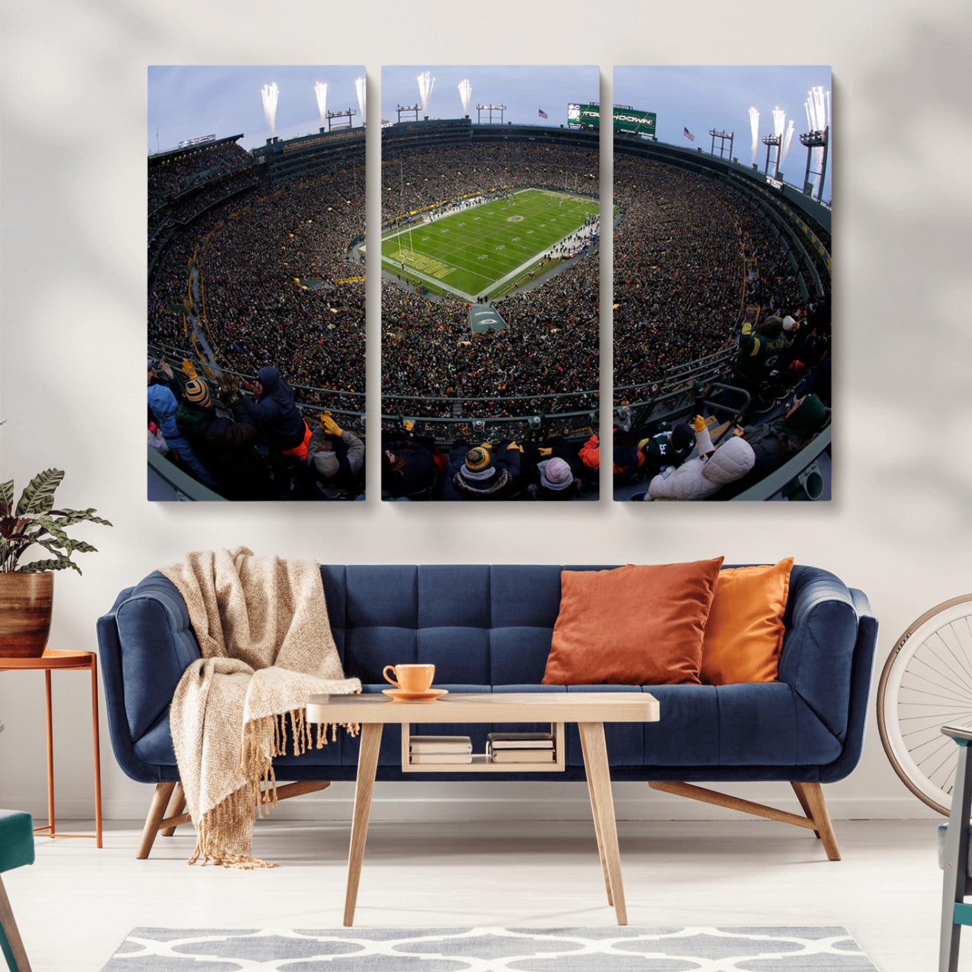 Wide fisheye view of a packed Lambeau Field stadium during an American football game. The crowd fills the stands, and fireworks are going off above the stadium lights. The scoreboard displays "Touchdown," and the field has "Packers" painted in the end zon