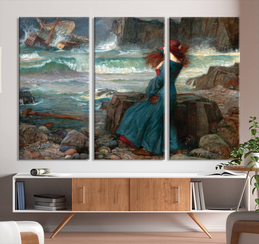 The Miranda by the Shore Wall Art Canvas Print depicts a woman in a blue dress standing by the sea, watching a shipwreck.