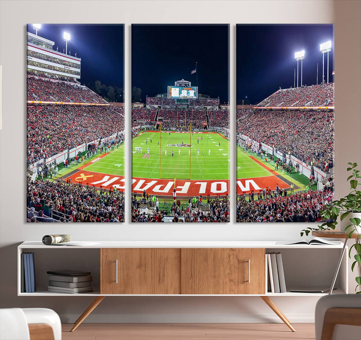 A NC State Wolfpack Football Team print of Carter-Finley Stadium at night features WOLFPACK illuminated brightly in the end zone grass.