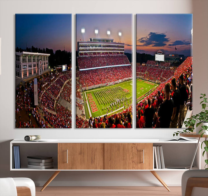 A print of a bustling Carter-Finley Stadium at dusk, featuring fans and a band, captures the essence of NC State Wolfpack football.