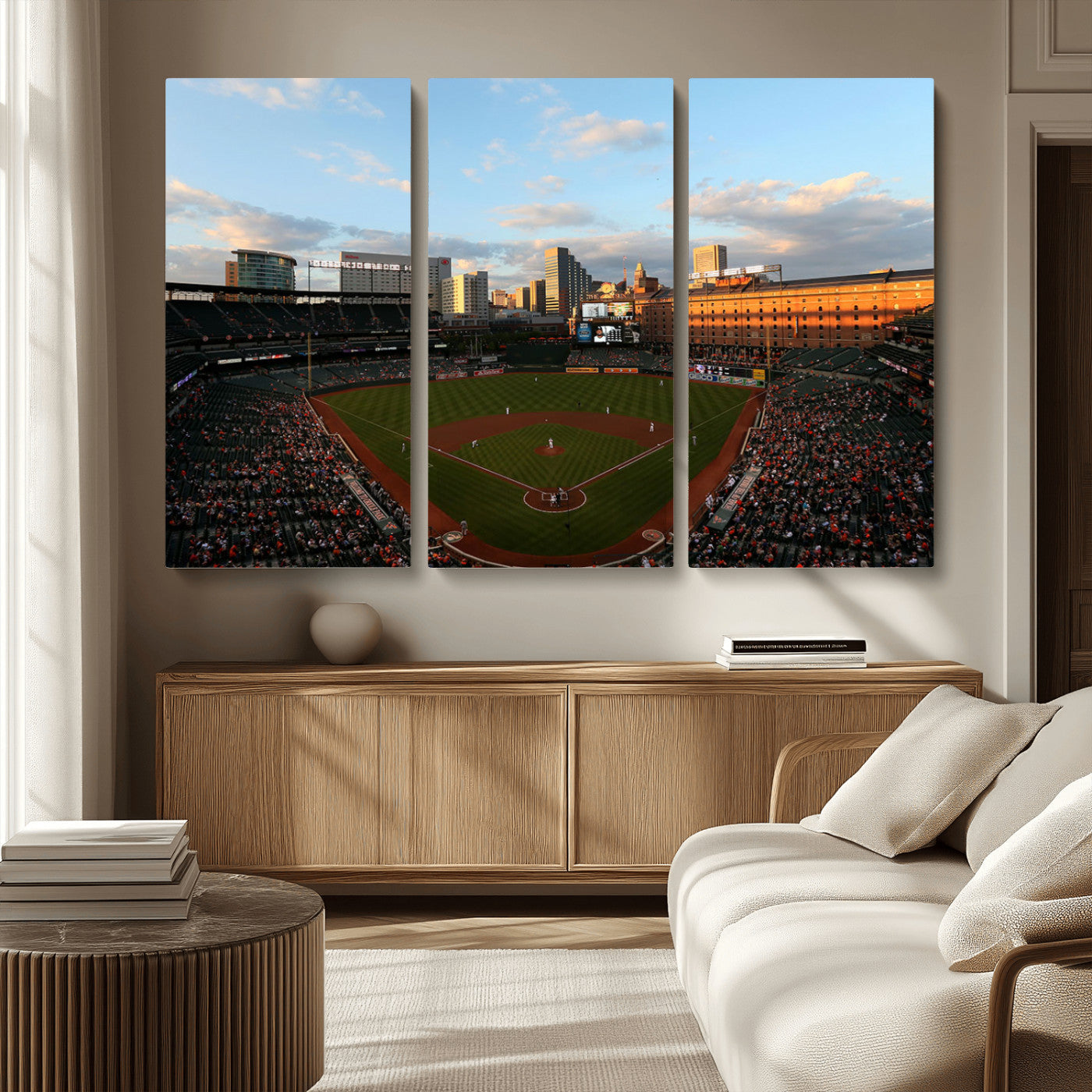 Aerial view of a baseball stadium at sunset with players on the field, fans in the stands, a city skyline in the background, and the setting sun casting warm light on the buildings.