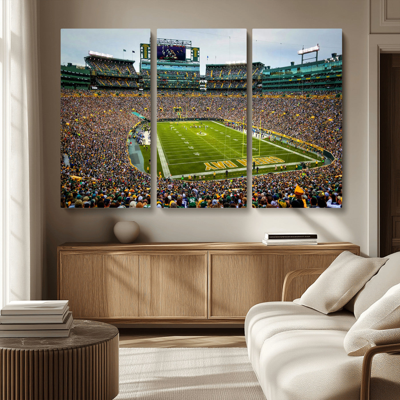 Packed football stadium with thousands of fans watching an American football game on a well-maintained field. The scoreboard displays "Lambeau Field," and players are lined up on the field. The stadium is surrounded by multiple tiers of seating filled wit