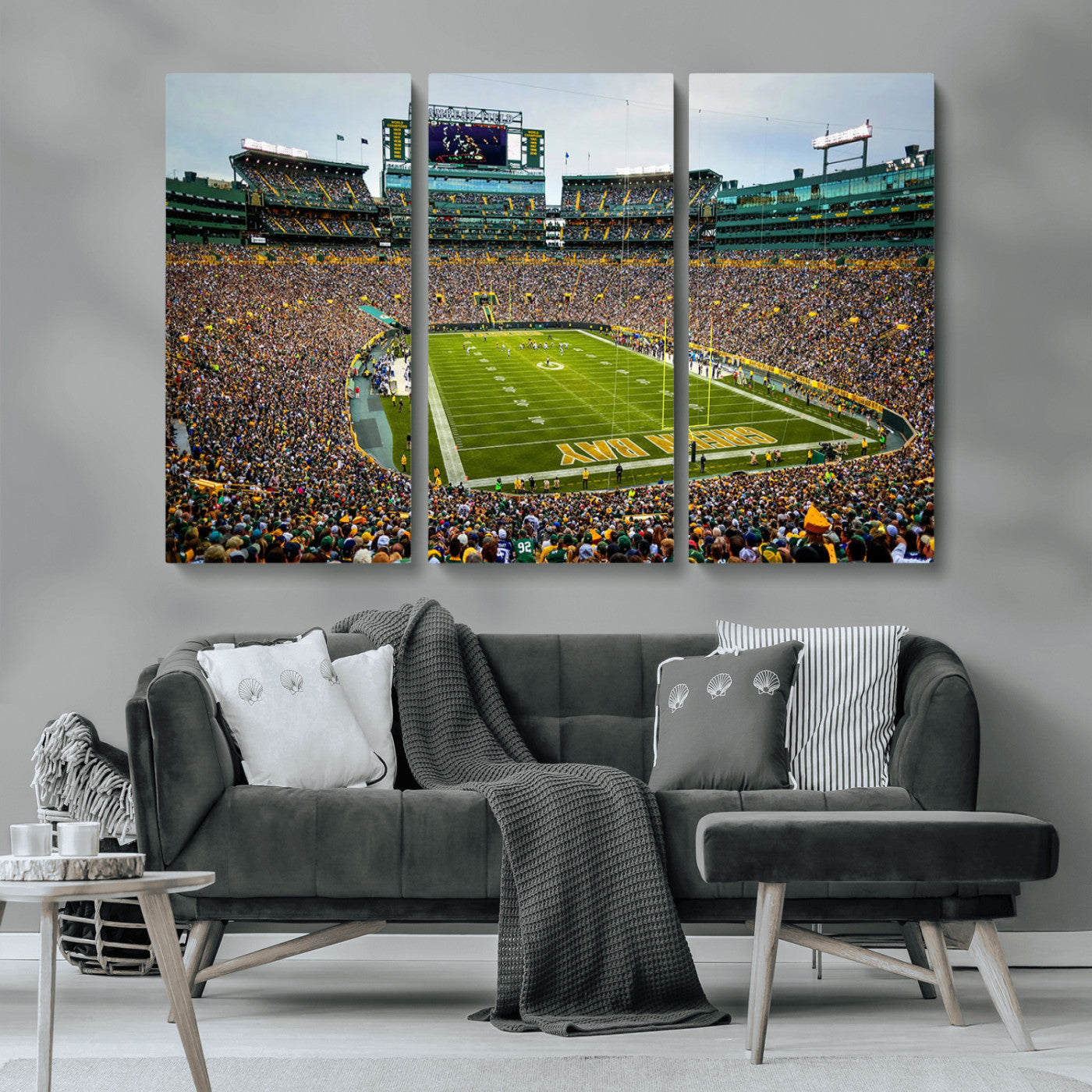 Packed football stadium with thousands of fans watching an American football game on a well-maintained field. The scoreboard displays "Lambeau Field," and players are lined up on the field. The stadium is surrounded by multiple tiers of seating filled wit