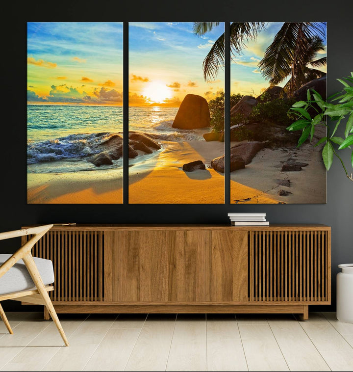 The Serene Tropical Beach Sunset Canvas Wall Art, a 3-panel giclee print, beautifully captures an ocean sunset with its depiction of palm trees and a coastal rock formation.