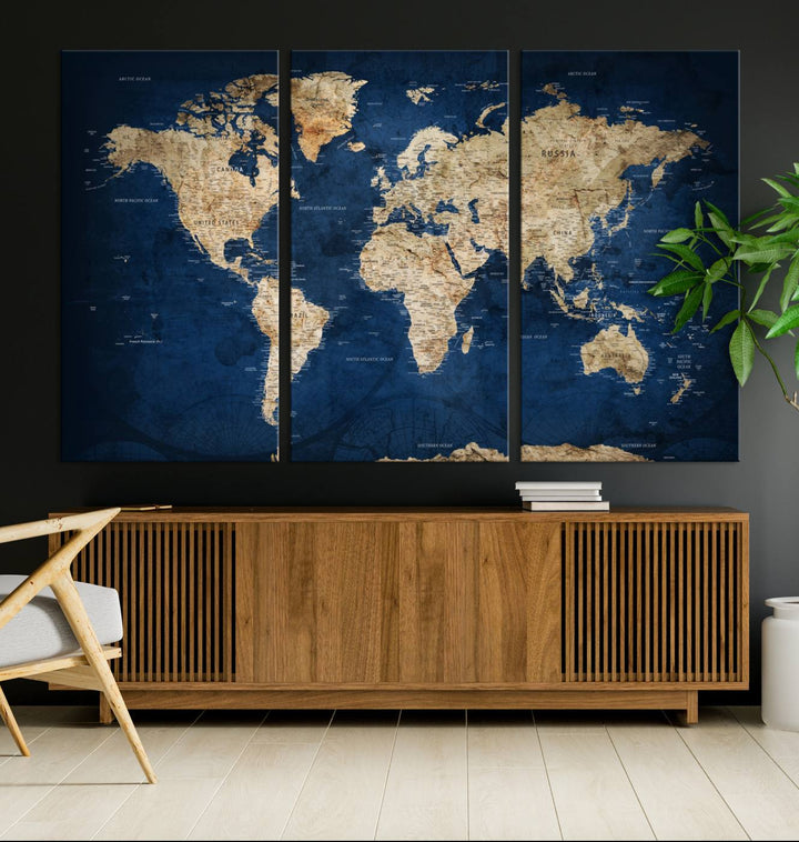 A large framed world map canvas print features beige landmasses set against a grunge-stained deep blue ocean background, creating an intriguing piece of wall art.