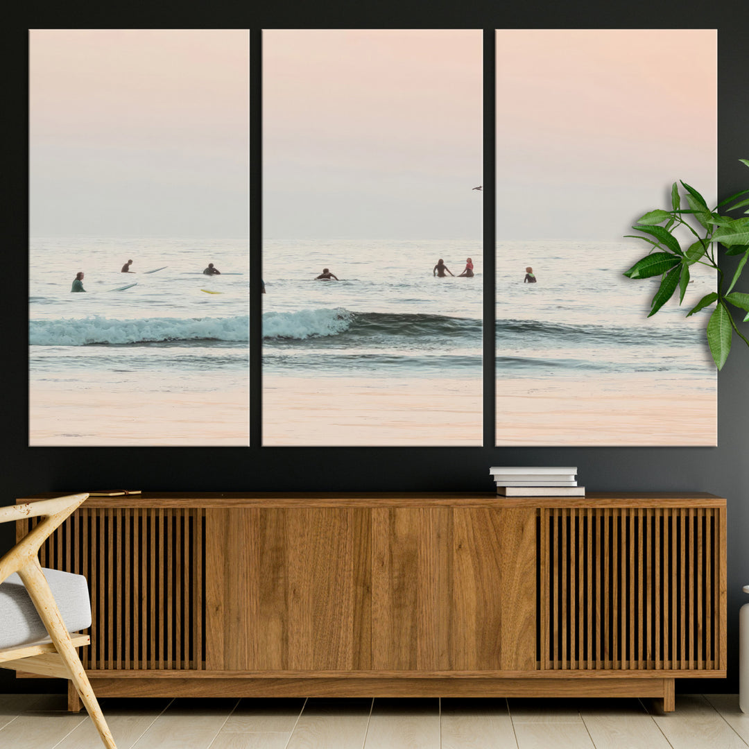 Dreamy photo of surfers waiting on soft pastel waves under a pink sunset sky, ideal for soft coastal minimalist or serene ocean-themed home decor.