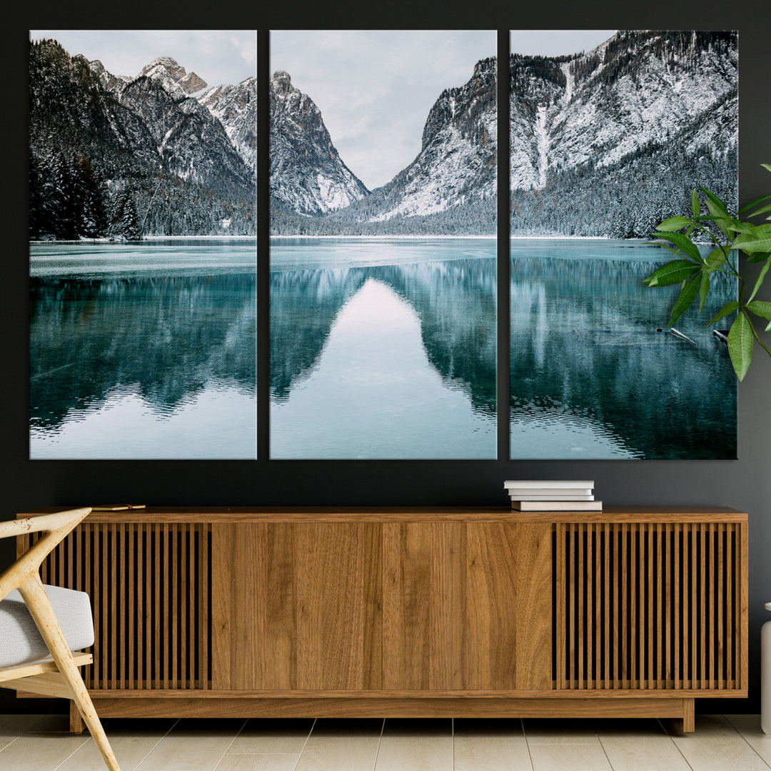 Crystal-clear alpine lake reflecting snow-covered mountains, surrounded by evergreen trees, creating a serene and tranquil winter landscape.