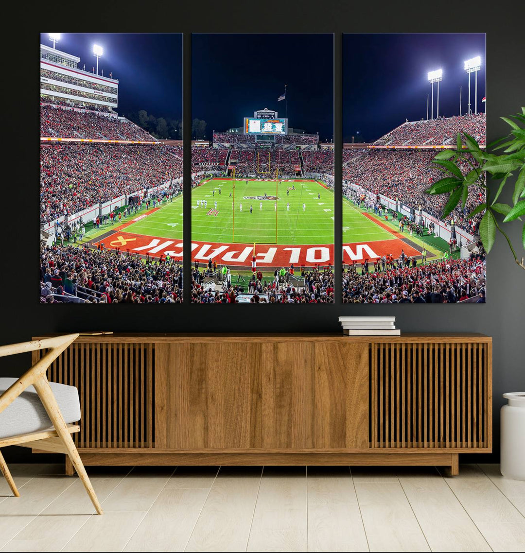 A NC State Wolfpack Football Team print of Carter-Finley Stadium at night features WOLFPACK illuminated brightly in the end zone grass.