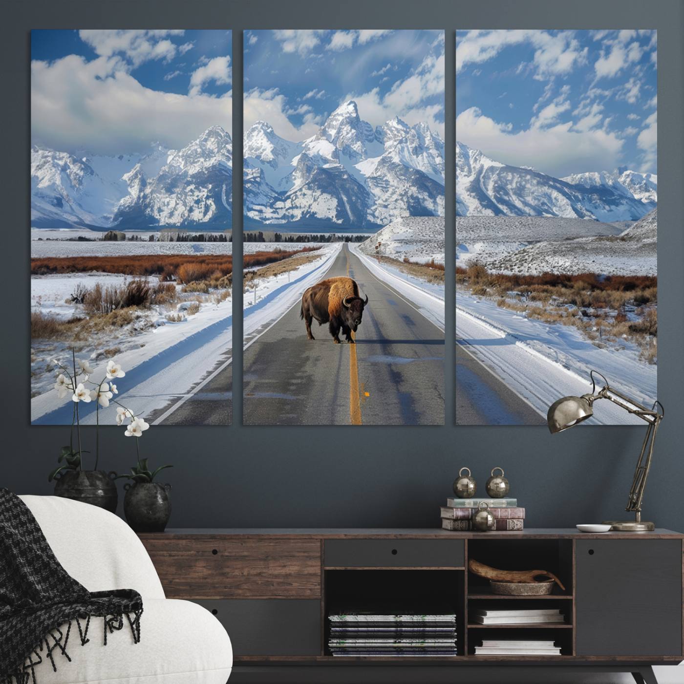 A powerful bison stands on a snow-dusted road beneath the towering peaks of the Grand Tetons, capturing the untamed beauty of America's winter wilderness.