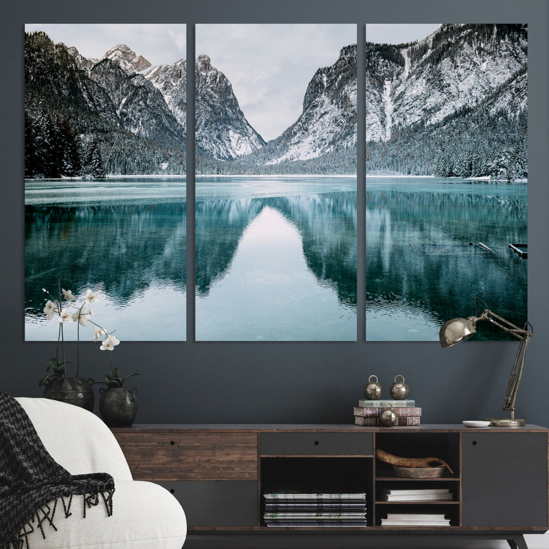 Crystal-clear alpine lake reflecting snow-covered mountains, surrounded by evergreen trees, creating a serene and tranquil winter landscape.