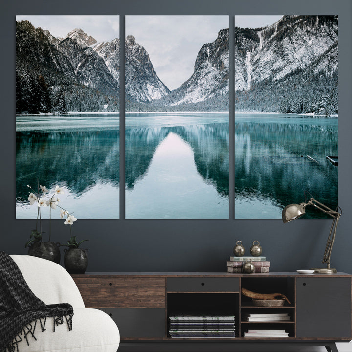 Crystal-clear alpine lake reflecting snow-covered mountains, surrounded by evergreen trees, creating a serene and tranquil winter landscape.