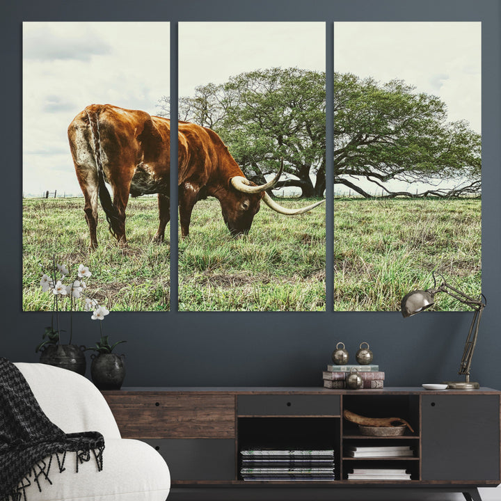 A Texas Longhorn grazing in a green pasture with a large tree in the background, evoking a rustic Western and farmhouse aesthetic.