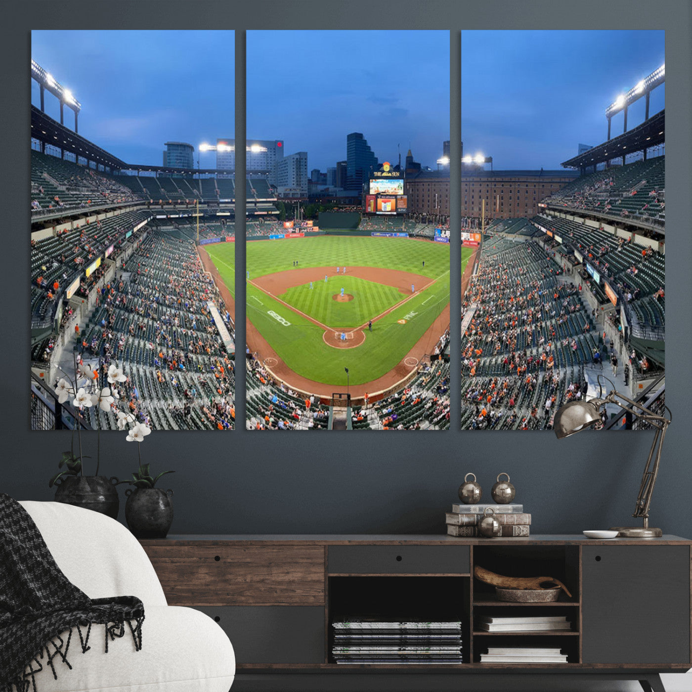 Wide panoramic view of a baseball stadium at dusk with players on the field, stadium lights illuminating the scene, and a sparse crowd of spectators in the stands.