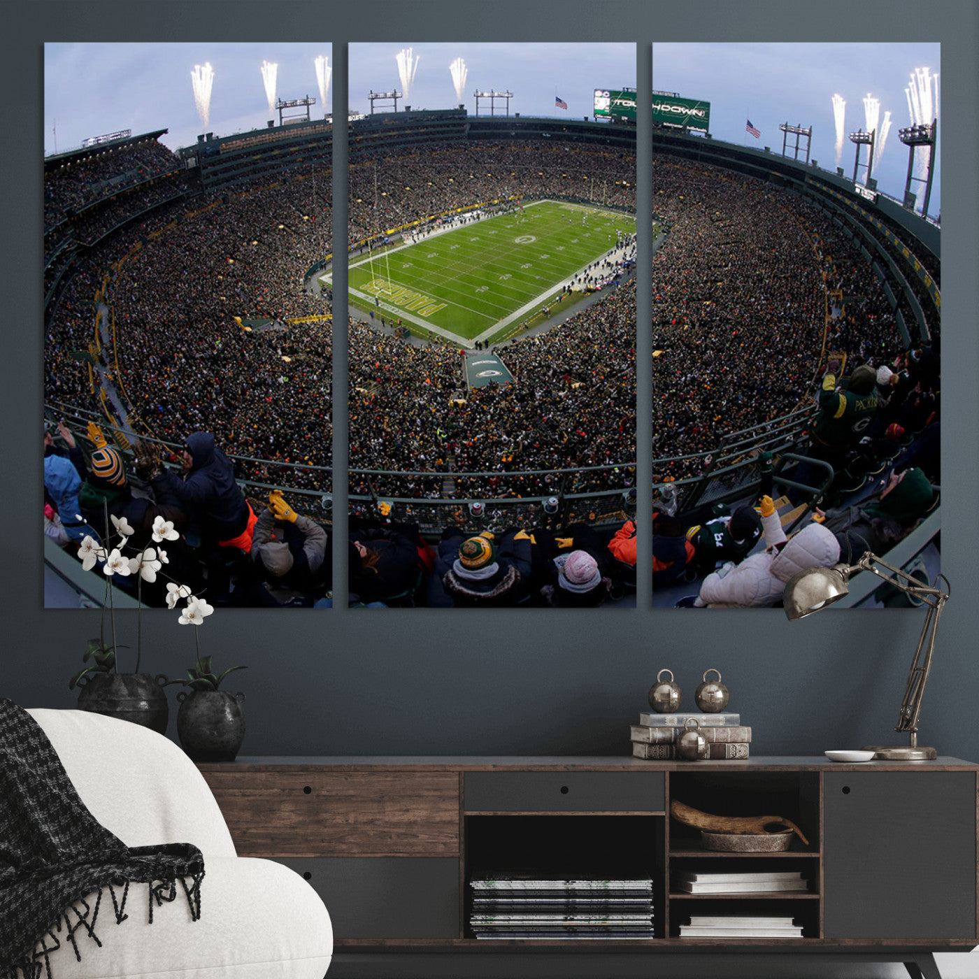Wide fisheye view of a packed Lambeau Field stadium during an American football game. The crowd fills the stands, and fireworks are going off above the stadium lights. The scoreboard displays "Touchdown," and the field has "Packers" painted in the end zon
