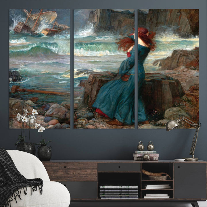 The Miranda by the Shore Wall Art Canvas Print depicts a woman in a blue dress standing by the sea, watching a shipwreck.