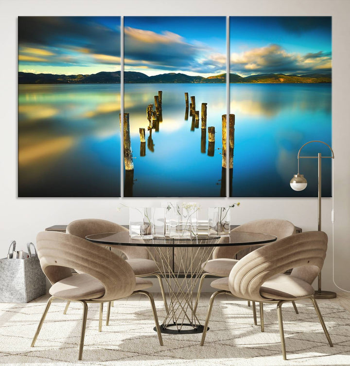 A triptych of a serene lake scene with old wooden pillars, blue sky, and clouds casts a coastal ambiance. The Sea Ocean Sunset Beach Wall Art Canvas Print reflects the soothing nature of the ocean.