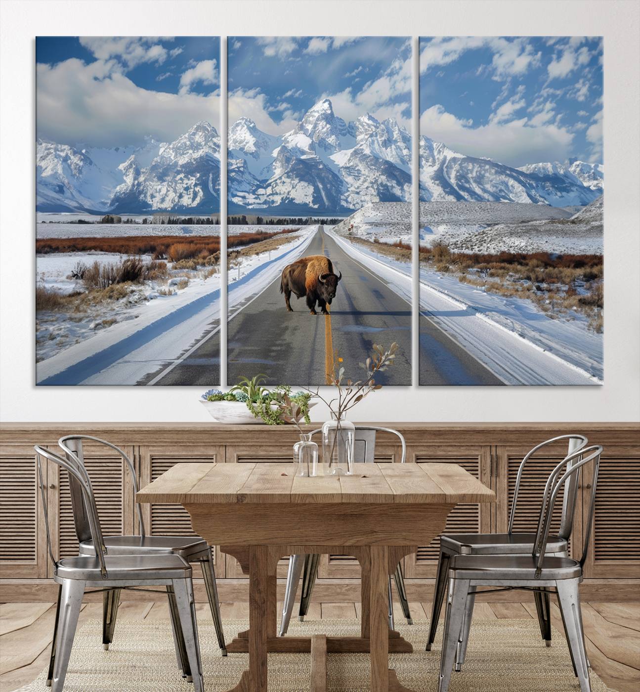 A powerful bison stands on a snow-dusted road beneath the towering peaks of the Grand Tetons, capturing the untamed beauty of America's winter wilderness.