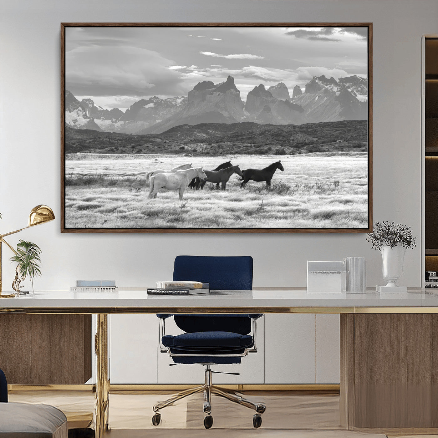 A black and white landscape of wild horses grazing in a vast grassland with towering mountains in the background, creating a moody and rustic western aesthetic.