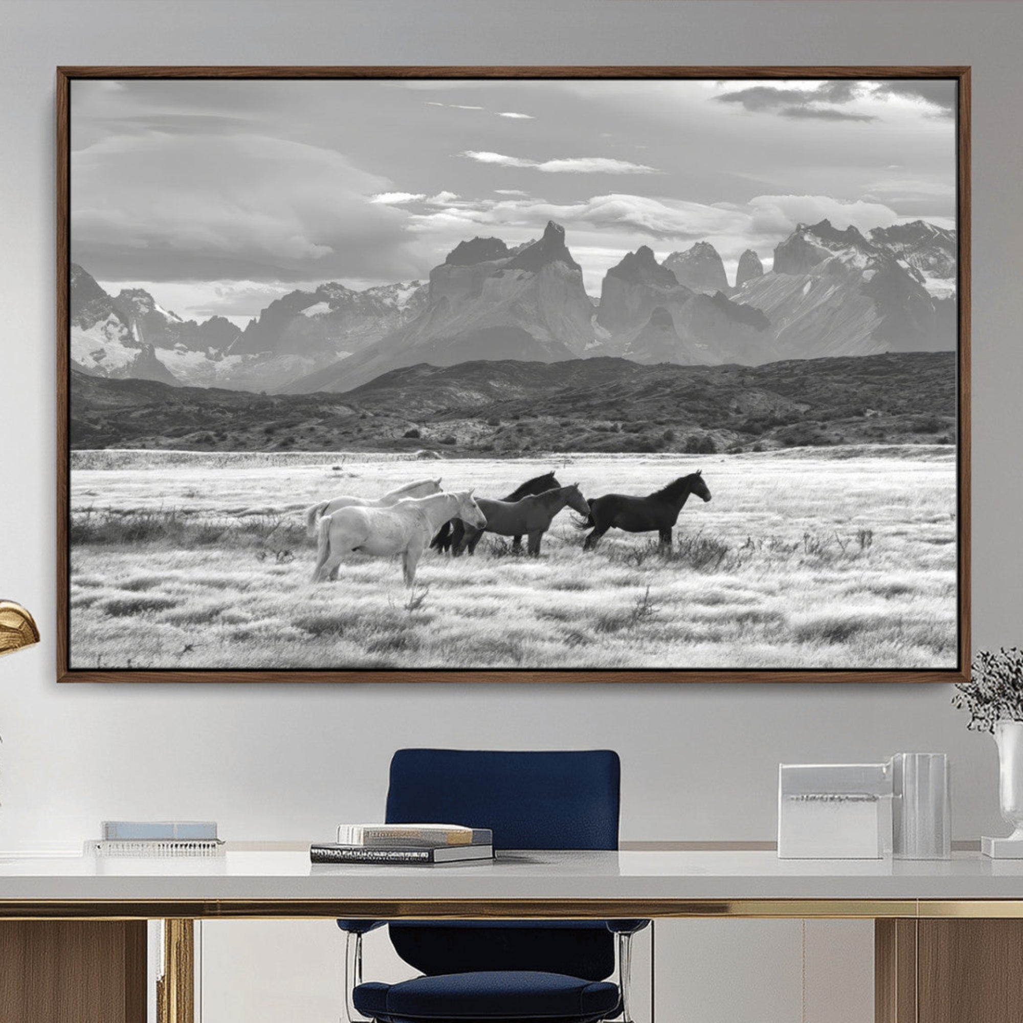 A black and white landscape of wild horses grazing in a vast grassland with towering mountains in the background, creating a moody and rustic western aesthetic.