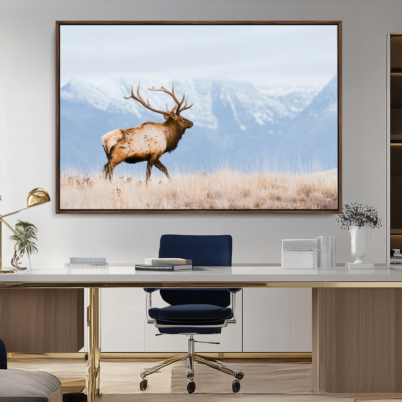 An elk walking on snowy grassland with majestic mountains in the background, ideal for rustic lodge or cabin wall decor.