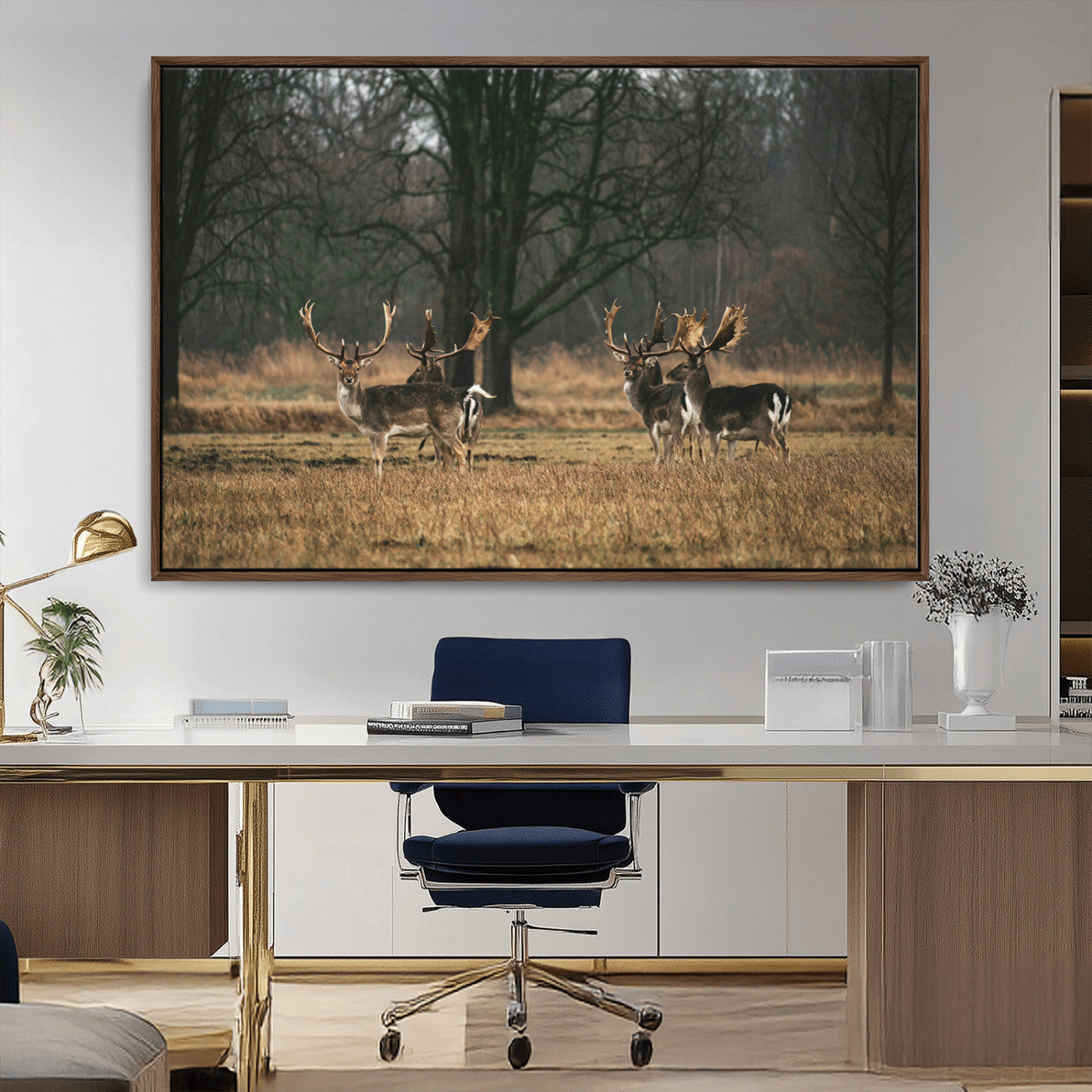 A group of majestic deer standing in a golden field with bare trees in the background, creating a peaceful woodland scene.