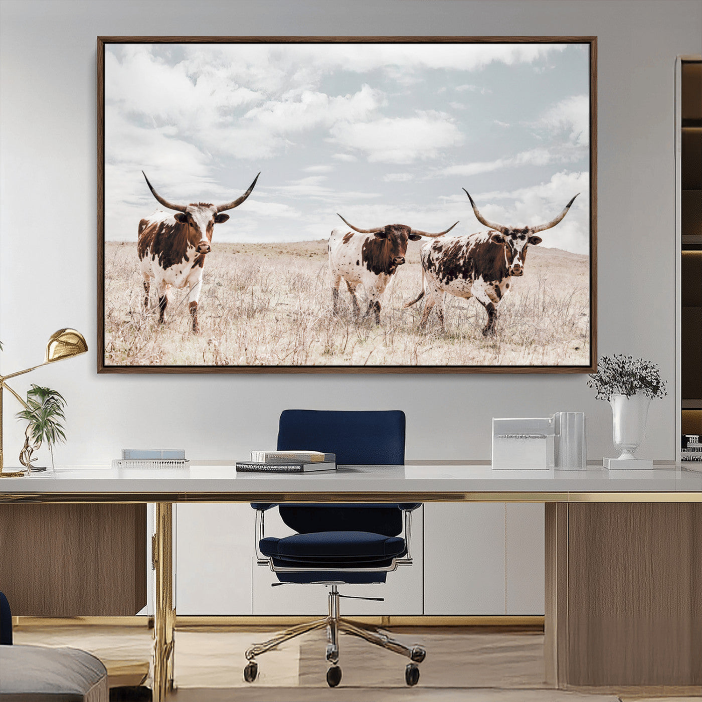 Three Texas Longhorn cattle walking through a dry grassy field under a partly cloudy sky.