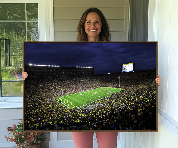 A painting of the packed Michigan Wolverines football stadium at night.