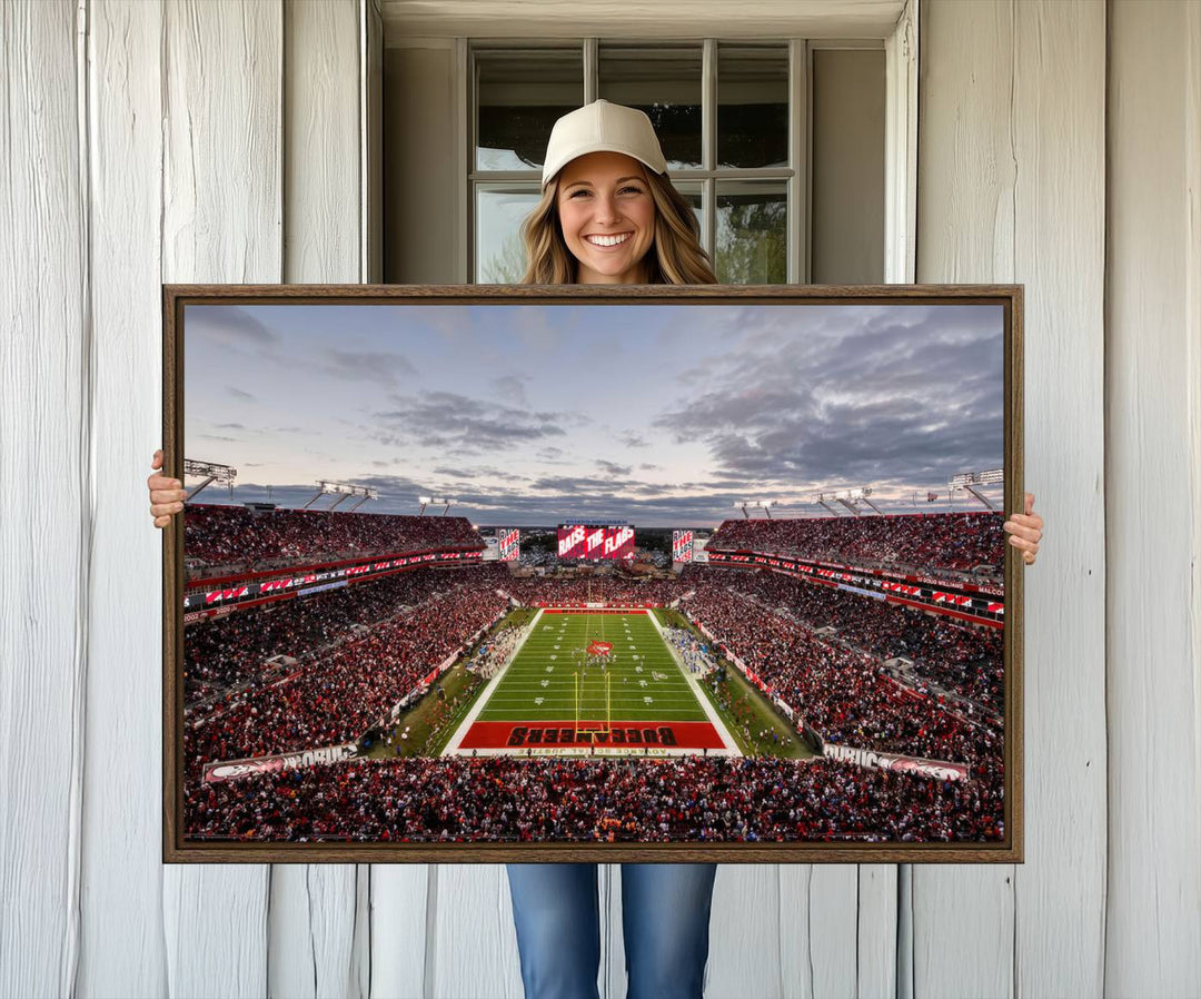 The wall art captures a stunning scene of Raymond James Stadium bathed in the warm hues of sunset. The sky, filled with clouds, provides a dramatic contrast to the vibrant lighting on the field, encapsulating the dynamic energy of a football game.