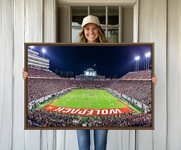 A NC State Wolfpack Football Team print of Carter-Finley Stadium at night features WOLFPACK illuminated brightly in the end zone grass.