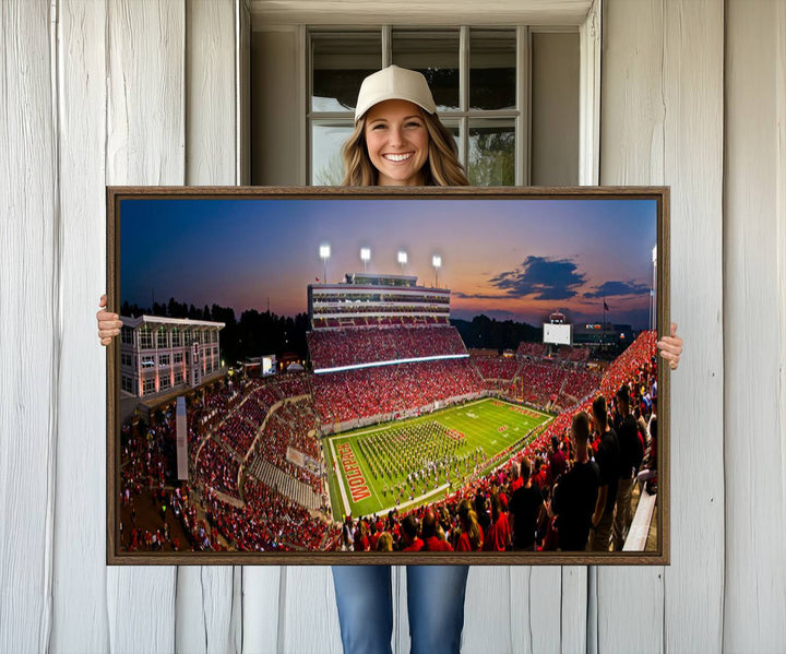 A print of a bustling Carter-Finley Stadium at dusk, featuring fans and a band, captures the essence of NC State Wolfpack football.