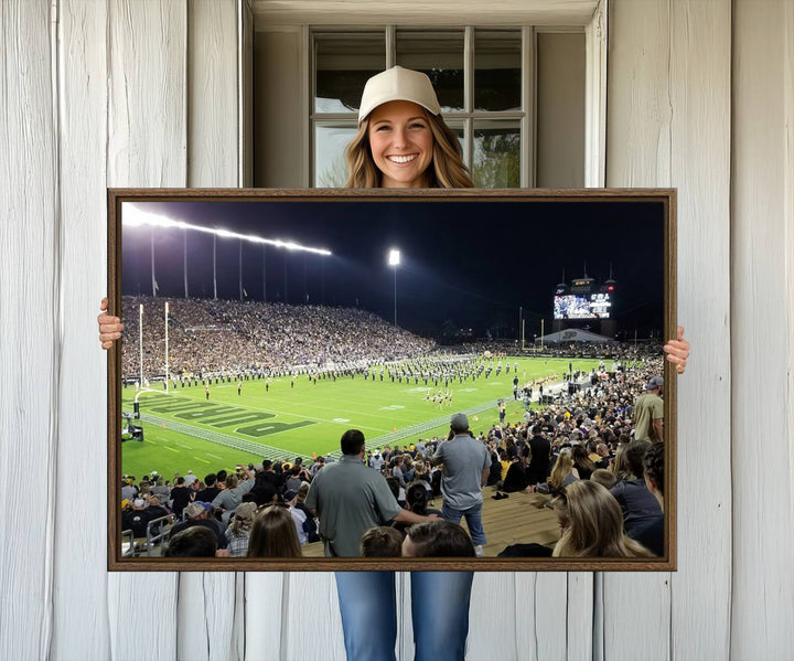 A painting depicting the Purdue Boilermakers football game at Ross-Ade Stadium is illuminated under gallery-quality lights.