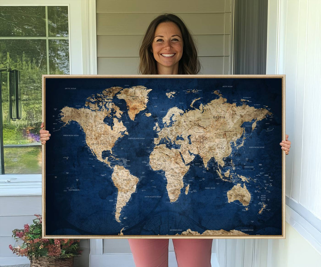 A large framed world map canvas print features beige landmasses set against a grunge-stained deep blue ocean background, creating an intriguing piece of wall art.