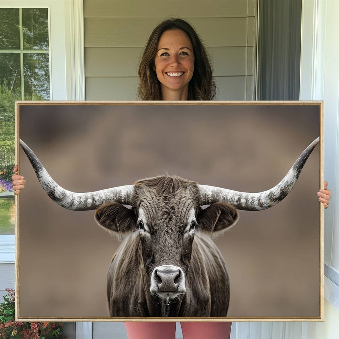 A close-up of a longhorn bull facing forward is featured in the Framed Texas Test-1, set against a blurred brown background.