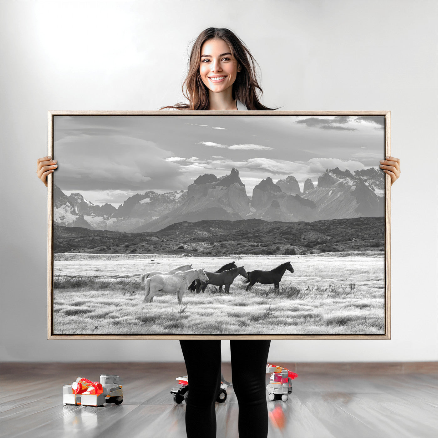 A black and white landscape of wild horses grazing in a vast grassland with towering mountains in the background, creating a moody and rustic western aesthetic.
