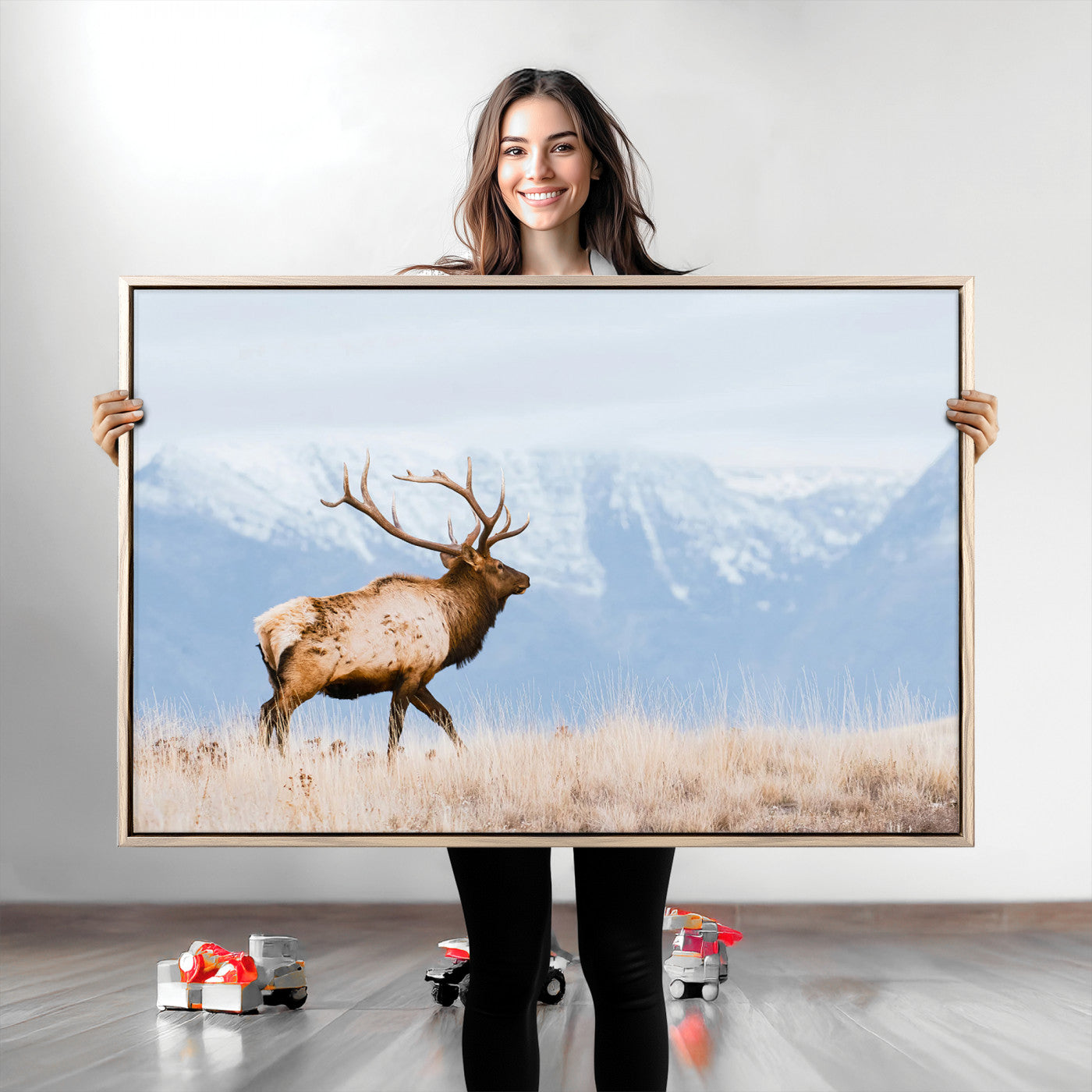 An elk walking on snowy grassland with majestic mountains in the background, ideal for rustic lodge or cabin wall decor.