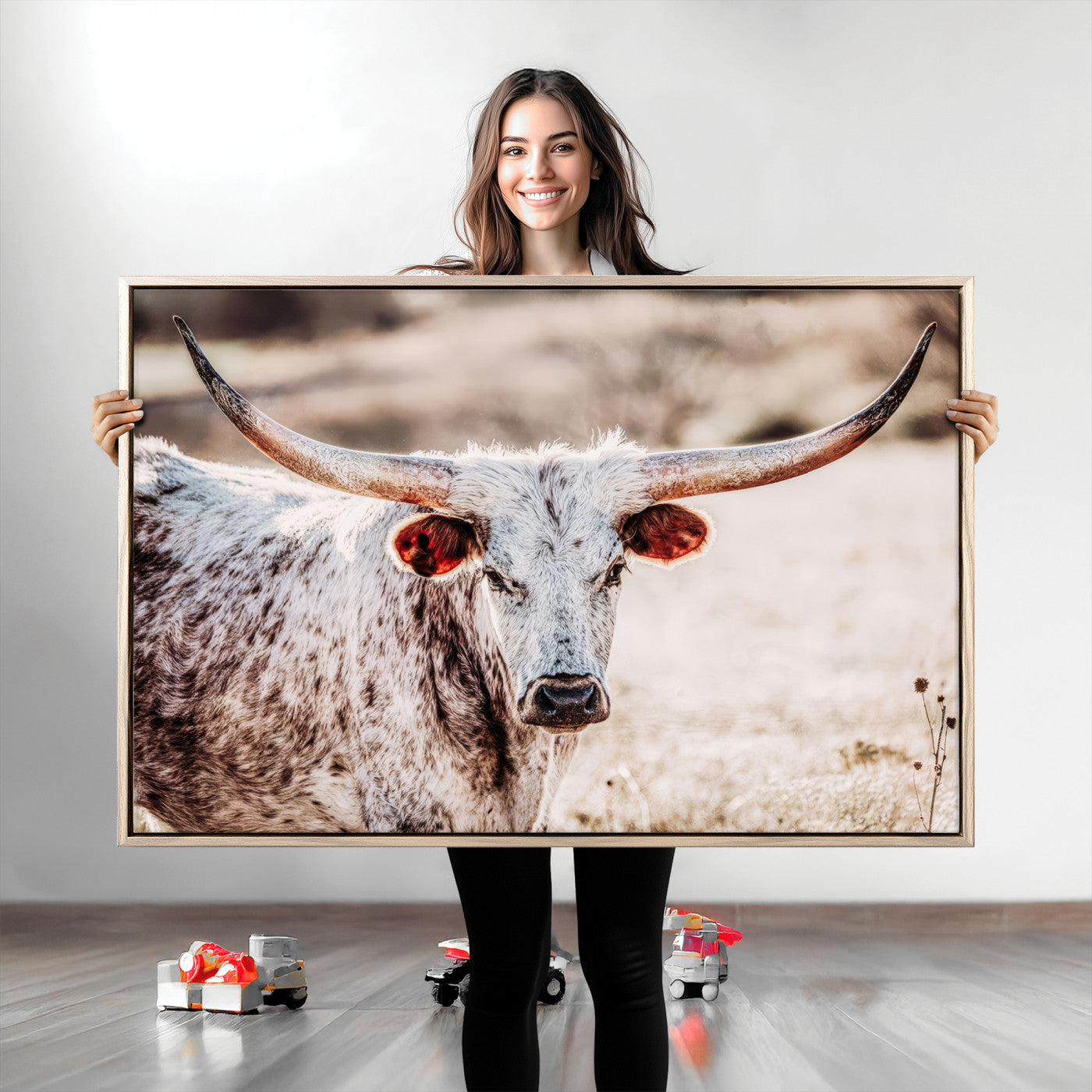 Close-up photograph of a white and brown speckled longhorn cow with very large, curved horns standing in a sunlit field with dry grass and blurred background.
