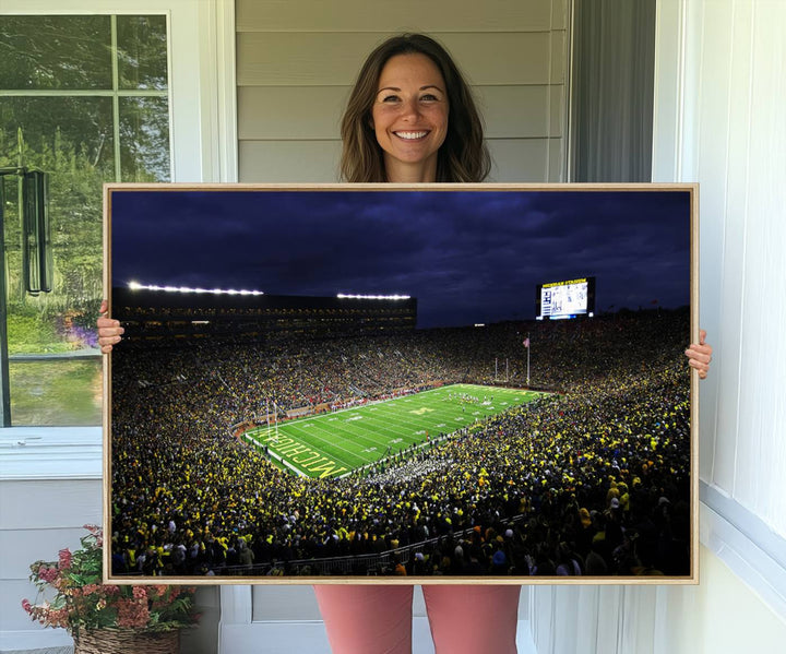A painting of the packed Michigan Wolverines football stadium at night.