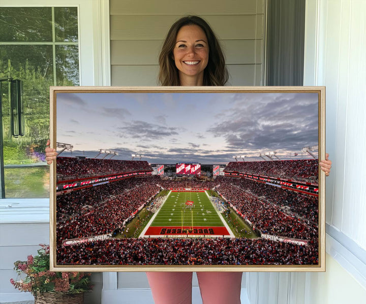 The wall art captures a stunning scene of Raymond James Stadium bathed in the warm hues of sunset. The sky, filled with clouds, provides a dramatic contrast to the vibrant lighting on the field, encapsulating the dynamic energy of a football game.