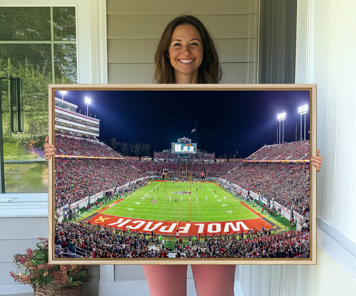 A NC State Wolfpack Football Team print of Carter-Finley Stadium at night features WOLFPACK illuminated brightly in the end zone grass.