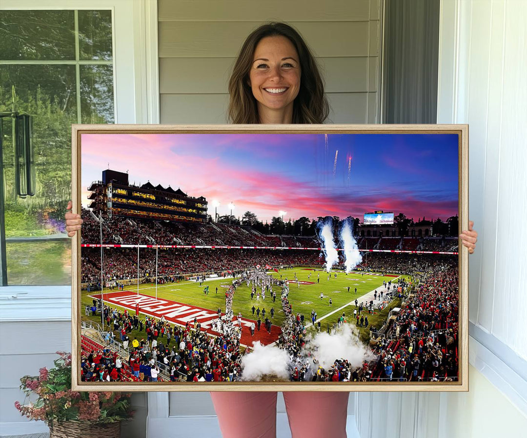 The wall art features a canvas print of the Stanford Cardinal football team, capturing players, fireworks, and smoke against the backdrop of a sunset at Stanford Stadium.