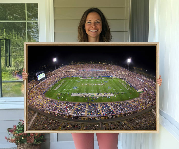 A large football stadium at night, featuring the UCONN Huskies, is depicted on the East Hartford Pratt & Whitney Stadium Wall Art Canvas Print.