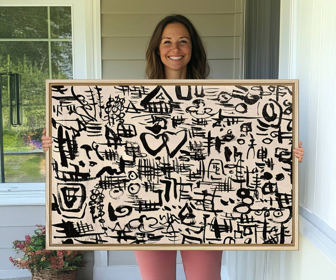 The Abstract Love and Chaos canvas is a museum-quality print featuring black symbols on a beige background, adorned with a heart and scribble design. It is framed to enhance its artistic appeal.