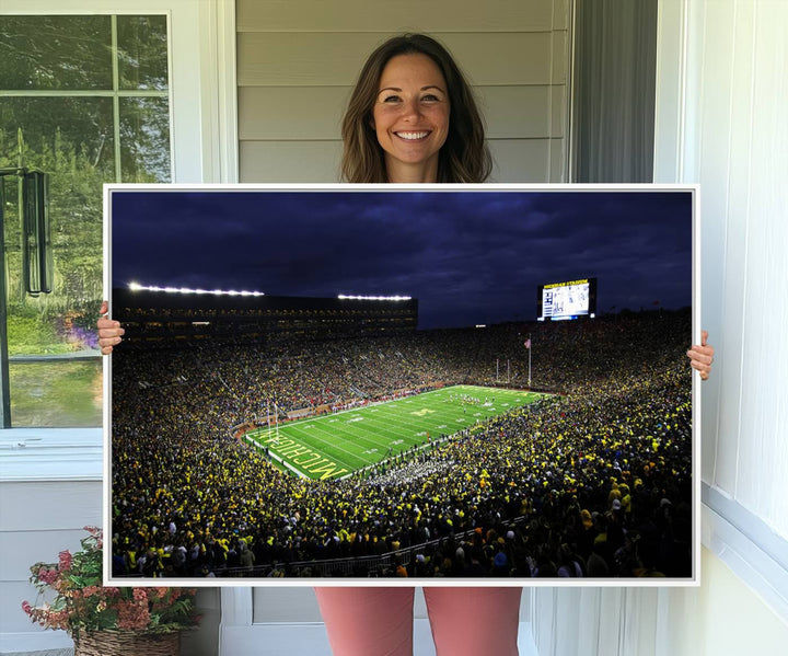 A painting of the packed Michigan Wolverines football stadium at night.