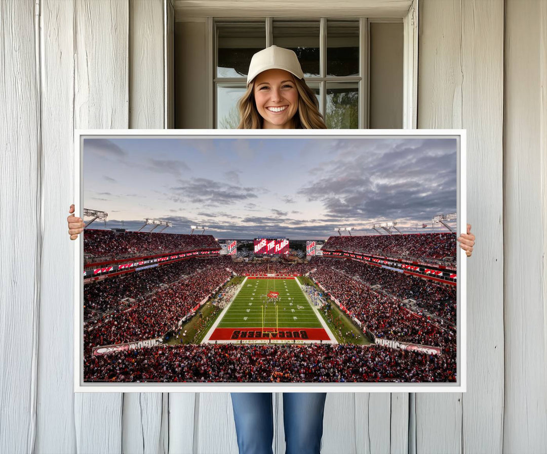 The wall art captures a stunning scene of Raymond James Stadium bathed in the warm hues of sunset. The sky, filled with clouds, provides a dramatic contrast to the vibrant lighting on the field, encapsulating the dynamic energy of a football game.