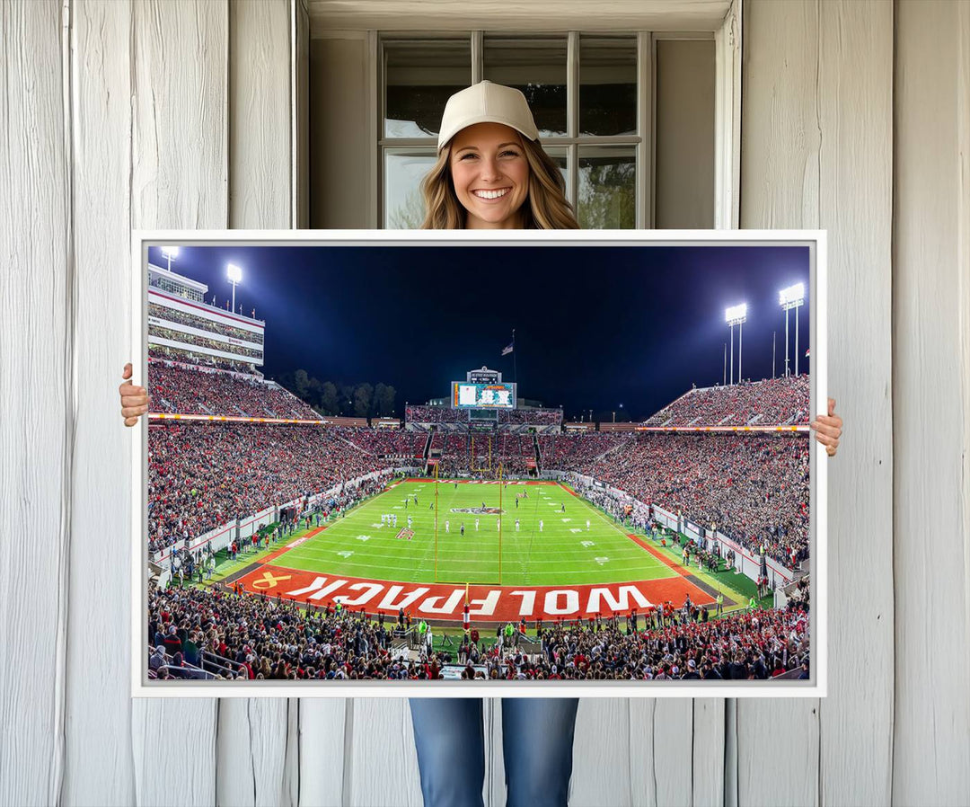 A NC State Wolfpack Football Team print of Carter-Finley Stadium at night features WOLFPACK illuminated brightly in the end zone grass.