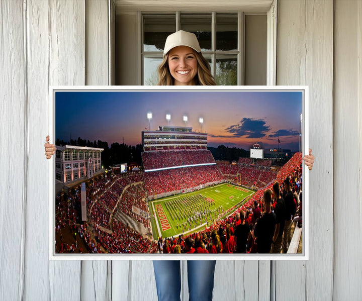 A print of a bustling Carter-Finley Stadium at dusk, featuring fans and a band, captures the essence of NC State Wolfpack football.